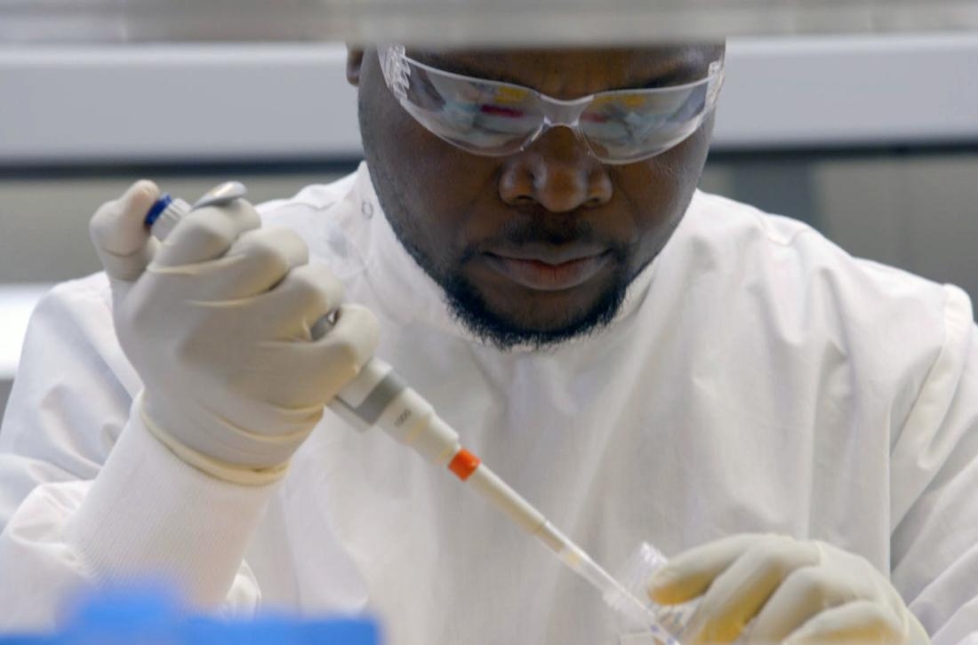 Dr Michael Selorm Avumegah pipetting at the bench in gown, gloves and safety glasses in the laboratory at the University of Queensland, Brisbane